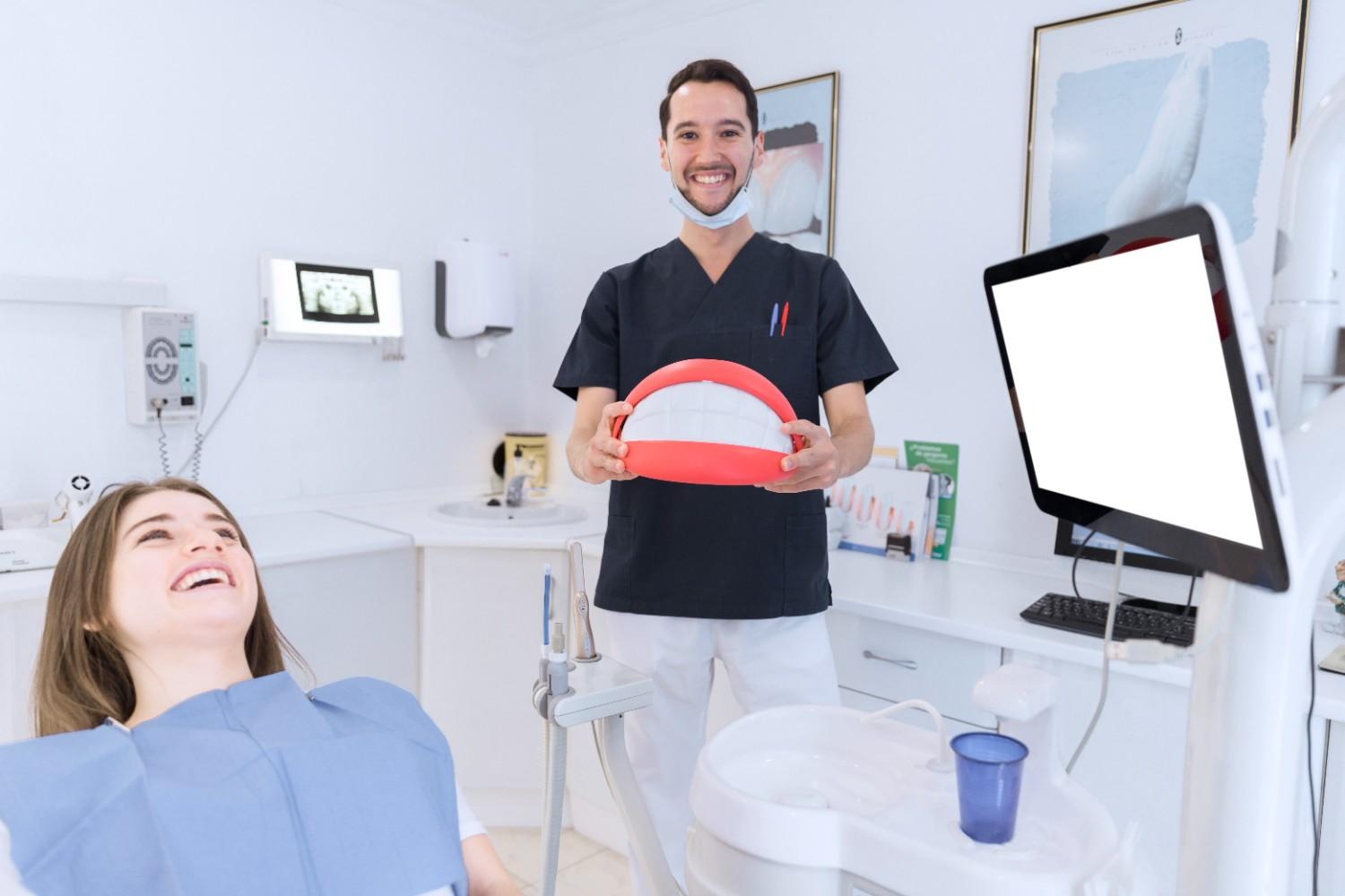 Dentist holding a dental model while a patient smiles in the chair.